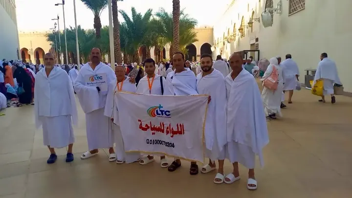 معتمرو اللواء بملابس الإحرام مع لافتة الشركة